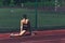 young woman doing deep lunge stretching on sports ground outdoors in summer.