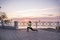 Young woman doing lunges, squats on warm-up in morning at sunrise by sea. Sportswoman in sportswear