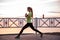 Young woman doing lunges, squats on warm-up in morning at sunrise by sea. Sportswoman in sportswear