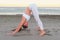 Young woman is doing yoga Adho mukha shvanasana on the sand beach at sunrise in autumn.