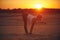 Young woman is doing yoga asana Ardha Uttanasana - Half Standing Forward Fold in the desert at sunset
