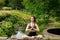 Young woman doing yoga. Girl sitting in the lotus position in the park near a small decorative lake