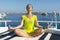 Young woman doing yoga meditation in lotus position on yacht. Peaceful young female practicing yoga on the yacht