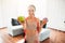 Young woman doing yoga workout in room during quarantine. Cheerful positive girl hold green apple and burger in hands