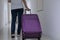 Young woman dragging purple luggage or baggage along the apartment`s corridor