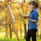 Young woman drawing a picture on canvas on an easel in nature, painter girl relaxing, a concept of lifestyle and a hobby
