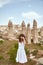 Young woman in dress expressing emotion while posing in front of high stone pillars in Cappadocia, Turkey