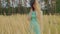 Young woman in dress and hat standing in wheat field. Pretty lady poses, standing in ears of wheat.