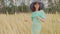 Young woman in dress and hat standing in wheat field. Pretty lady poses, standing in ears of wheat.