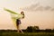 Young woman in dress making gymnastic pose and holding yellow cloth on summer day with field landscape at background