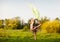 Young woman in dress making gymnastic pose and holding yellow cloth on summer day with field landscape at background