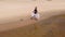 A young woman in a dress runs along the beach. Aerial shoot