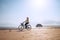 Young woman dressed light summer clothes riding old vintage bicycle with front basket on the lonely low tide ocean white sand