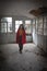 Young  woman dressed in red walking in an abandoned and colapsing room