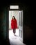 Young woman dressed in red walking through the open door of an abandoned room