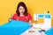 Young woman dressmaker sewing in her studio, being frustrated because she making mistake, sitting with opened mouth, holds