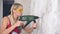 A young woman is drilling a wall with an electric hammer or drill