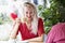 Young woman drinks coffee and laughs. Beautiful blonde with long hair in a red dress on the terrace of a summer cafe