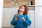 Young woman eating chocolate from a jar while sitting on the wooden kitchen floor. Cute ginger girl indulging cheeky face eating