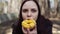 Young woman eating doughnut in woods. Casual young brunette in jacket sitting on log in woods and eating delicious glazed doughnut