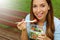 Young woman eating salad on lunch break in city park living healthy lifestyle. Happy smiling brazilian girl eating outdoor