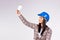 A young woman electrician in a blue helmet holds up an LED lamp in her hands like an idea for your advertisement. Gray