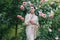 Young woman enjoying by blooming climbing pink rose in garden