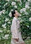 Young woman enjoying with closed eyes by blooming climbing white rose in garden