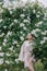 Young woman enjoying with closed eyes by blooming climbing white rose in garden