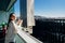 Young woman enjoying view on a sunny day with cup of coffee/tea on balcony in apartment in industrial/business area.Positive young