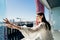 Young woman enjoying view on a sunny day, opening up a window on balcony in apartment in industrial/business area.Positive young