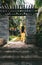 Young woman enters in the old stone arch on a tropical park with palm trees on a sunny morning