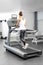 A young woman in an exercise room is running on an automatic treadmill.