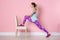 Young woman exercising with chair near color wall