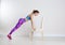 Young woman exercising with chair near white wall