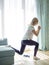 Young woman exercising at home in a living room. crouching using a couch. Full length side view photo, cross fit