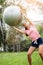 Young woman exercising with pilates ball in the park. Yoga instructor holding fitness ball over her head and training