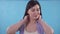 Young woman experiences pain in her neck standing on a blue background