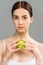 Young woman with face scrub on skin holding apple  on grey