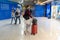 Young woman in facial protective mask with red suitcase and backpack walking in airport