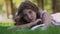 Young woman with fair hair lies on green grass near book
