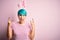 Young woman with fashion blue hair wearing easter rabbit ears over pink background shouting with crazy expression doing rock