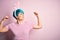 Young woman with fashion blue hair wearing easter rabbit ears over pink background showing arms muscles smiling proud