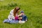 A young woman feeding a baby from spoon fruit puree on the green grass