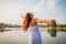 Young woman feeling free and happy raising arms and spinning around by summer river at sunset