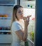 Young woman felling hungry at night standing on kitchen and eating pizza. Concept of unhealthy eating and nutrition