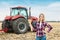 A young woman in a field on a background of a tractor with spike of wheat in her hands