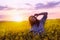 Young woman in a field of oil rapeseed in bloom in sunset. Freedom and ecology concept.