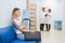 Young woman filling nervous sitting at hospital corridor waiting while two doctors talking on a backgroud