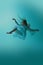 Young woman floats elegantly, gracefully midair in flowing vintage teal dress against serene aqua background.